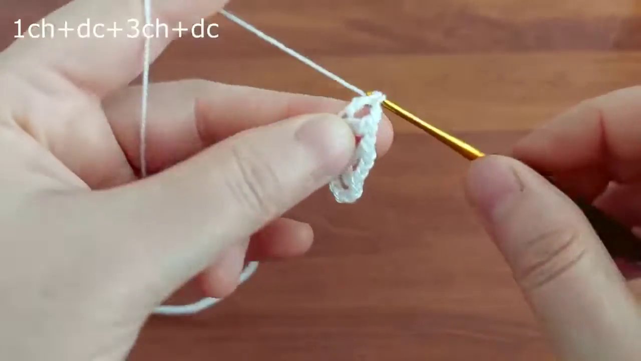 Đôi tay đang thực hiện mũi móc đầu tiên trên nền gỗ ấm áp.
