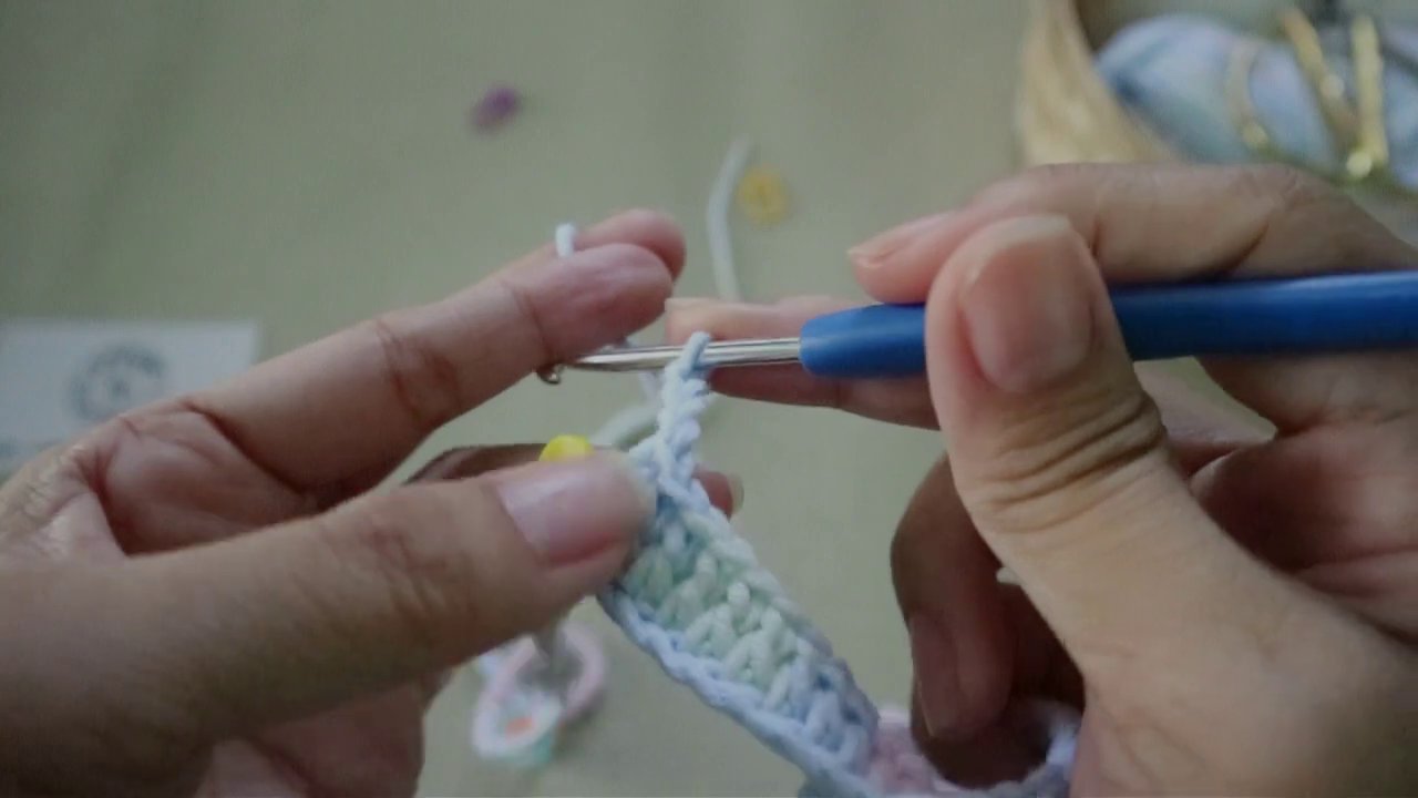 Cảnh tay người đang tỉ mỉ luồn kim qua các vòng nhỏ li ti.