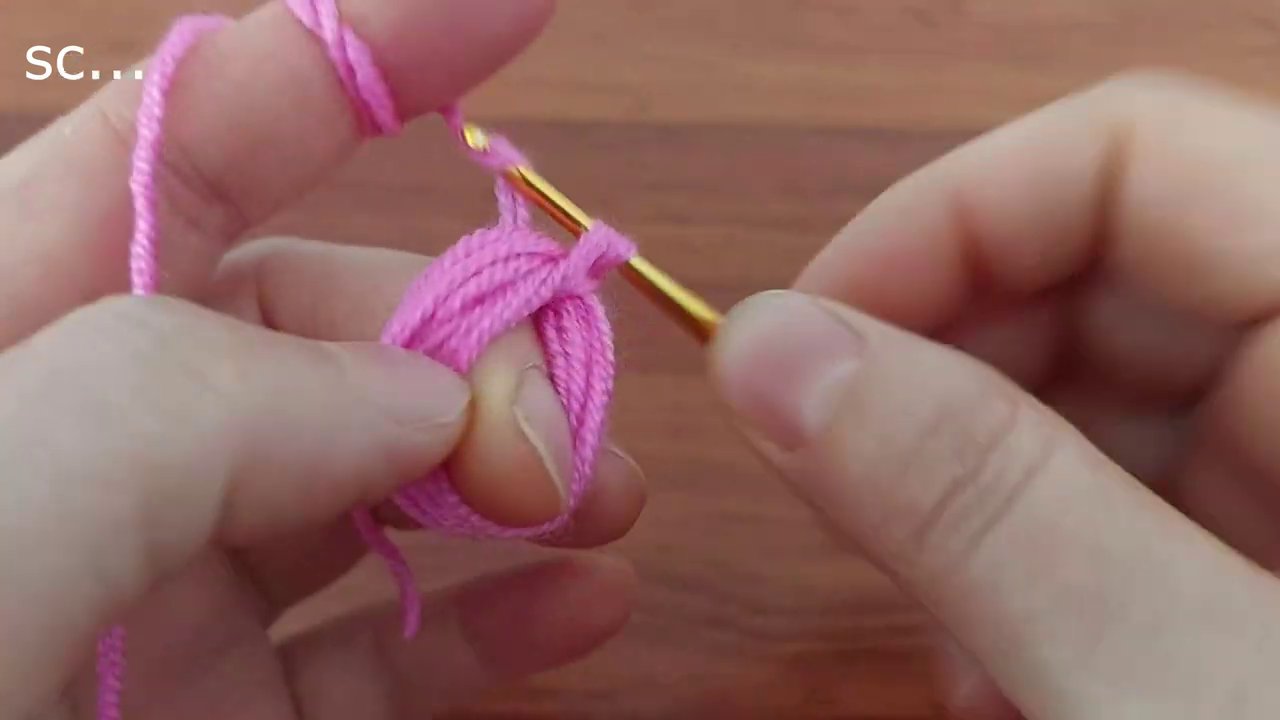 Bàn tay cầm kim và sợi len hồng khi bông hoa crochet dần thành hình.