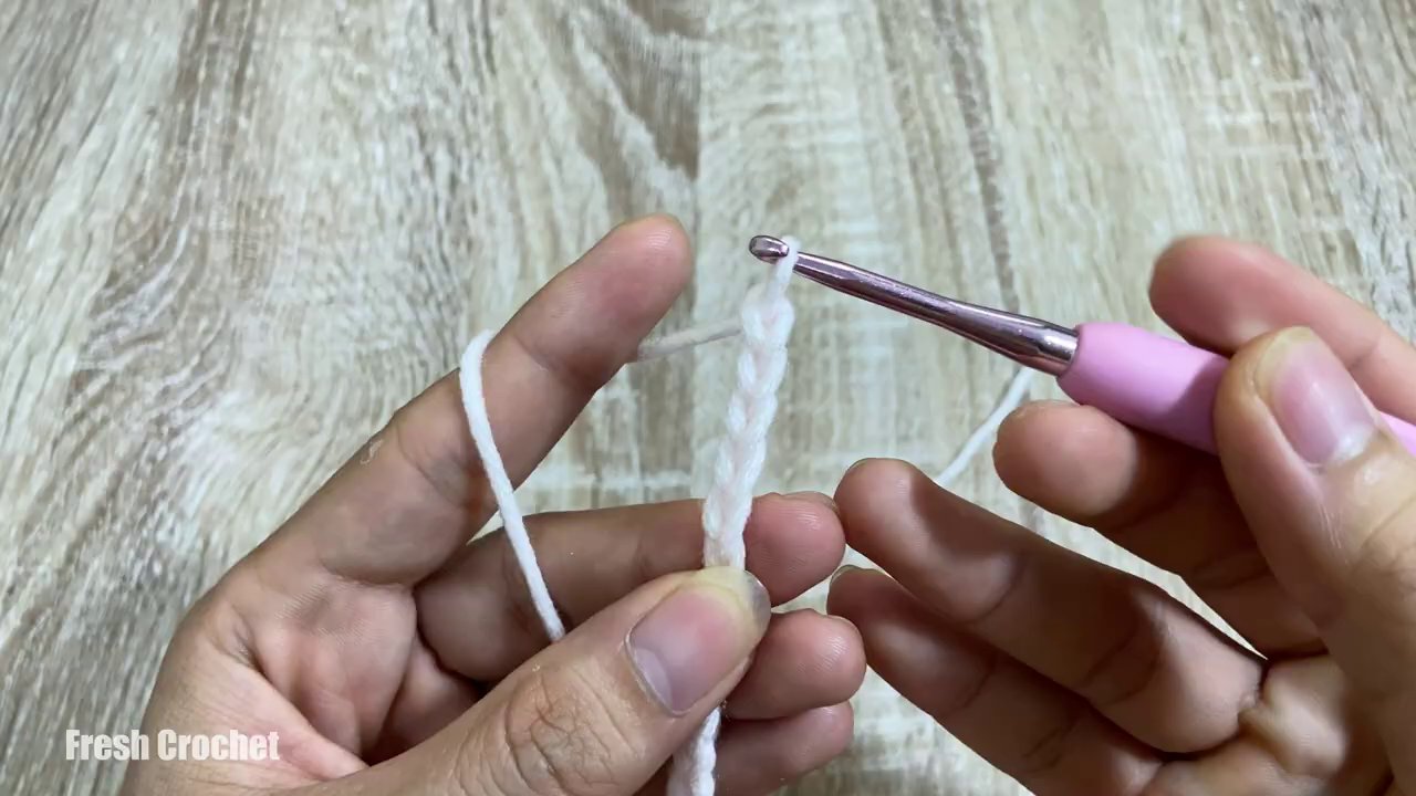 Tay cầm kim móc đang thực hiện mũi đơn trên một mảnh len màu xanh lá.