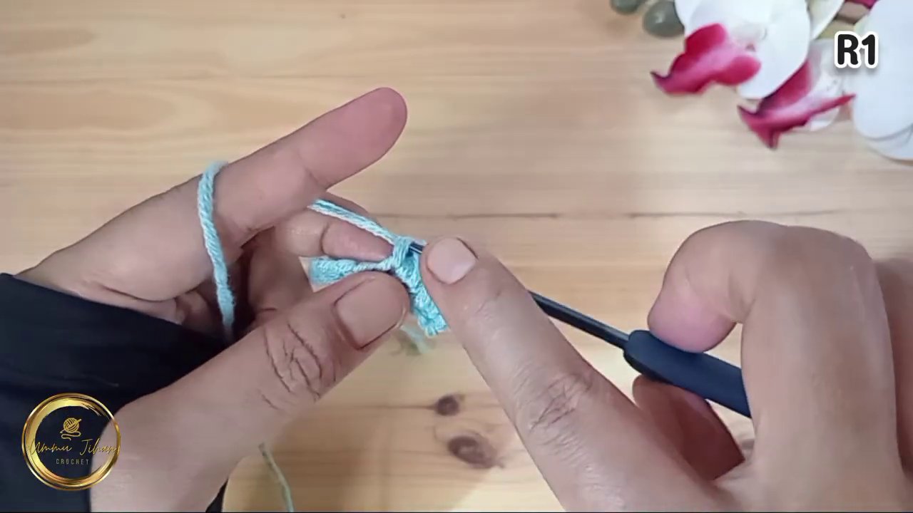 Tay đang thực hiện bước kéo len qua vòng đầu tiên của mũi móc đơn.