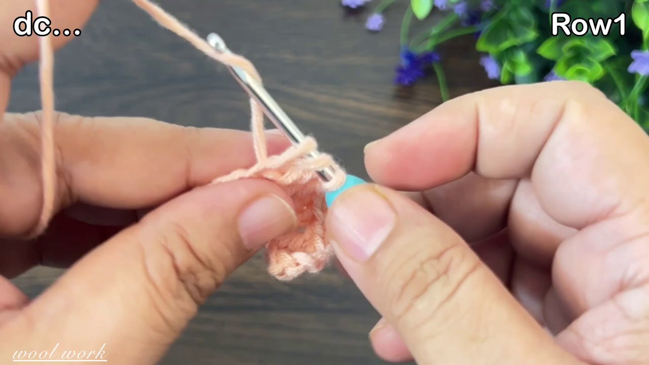 Một đôi ta y đang cầm kim móc và cuộn len, bên cạnh là tờ hướng dẫn móc có nhiều ký hiệu phức tạp.