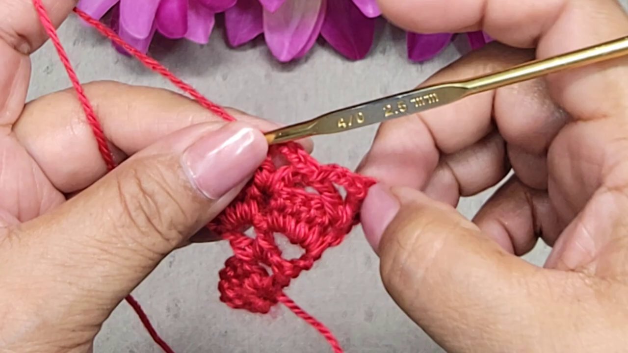 Một người phụ nữ đang móc len với nụ cười thoải mái, tập trung và o sản phẩm.