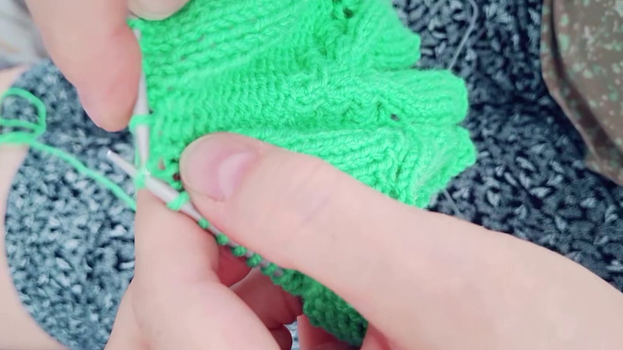 Một người đang cầm trên ta y sản phẩm móc len đầu tiên của mình, nụ cười rạng rỡ trên môi.