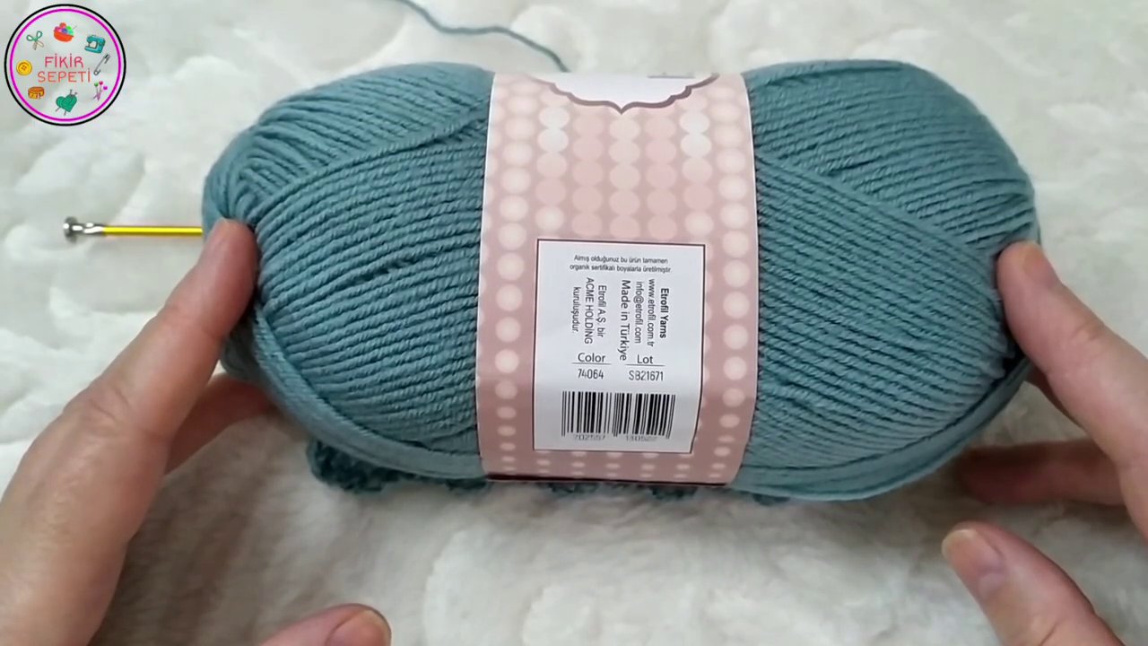 Một bàn ta y đang cầm kim móc và sợi len, chuẩn bị thực hiện mũi móc đầu tiên.