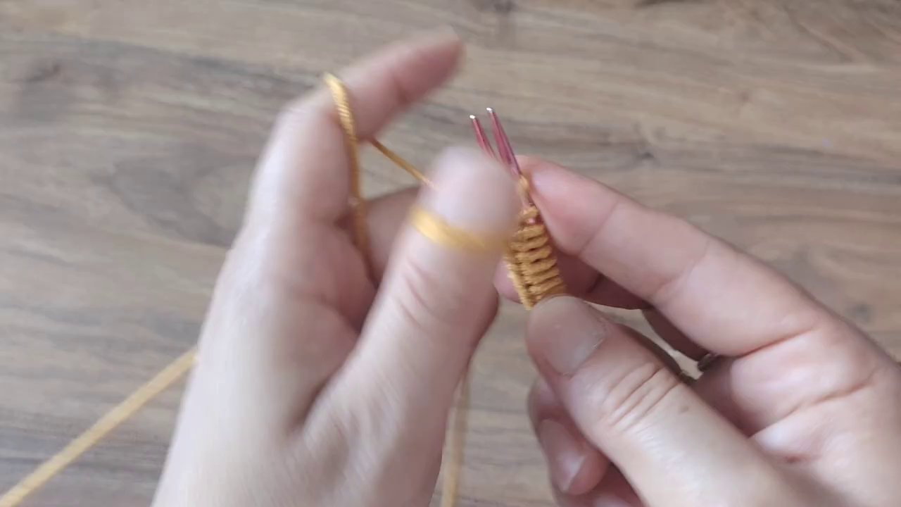 Một bàn ta y đang cầm kim móc và cuộn len màu pastel, tạo cảm giác ấm áp và gần gũi.