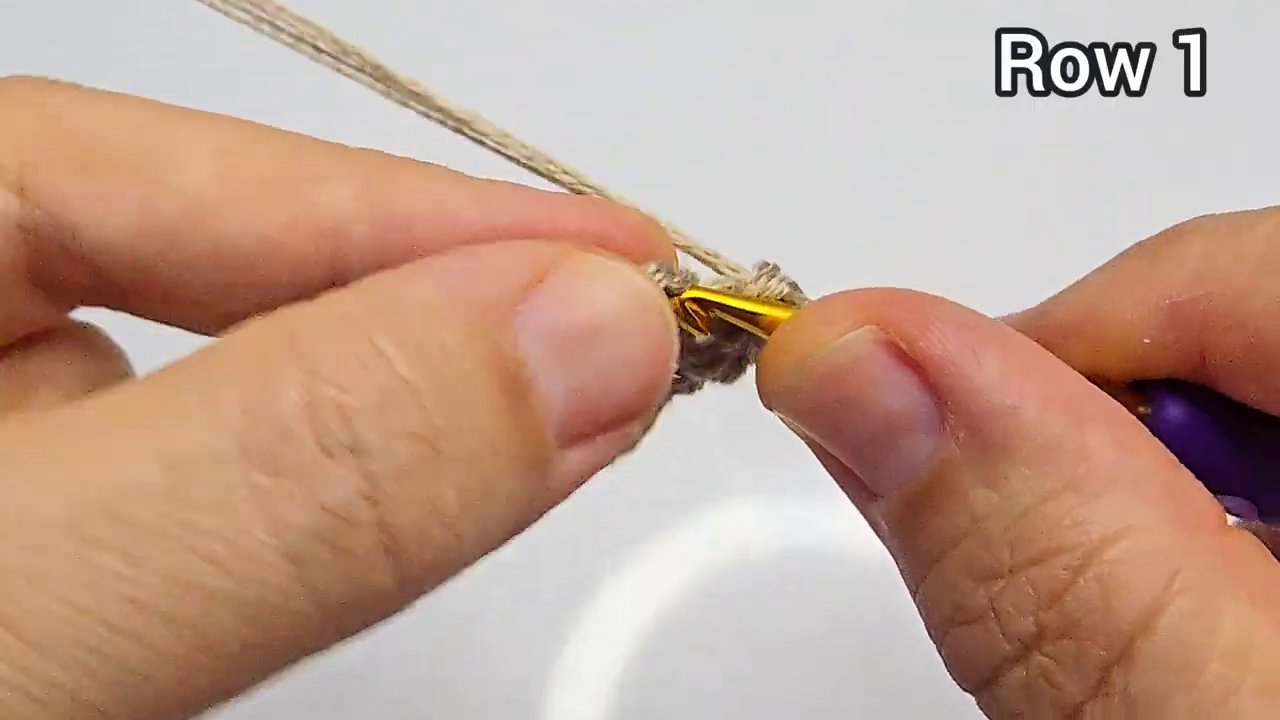 Tay cầm que móc, một vòng len màu hồng được đánh dấu bằng một sợi len khác ở mũi đầu hàng.
