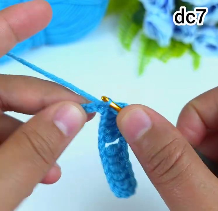Hai bàn ta y đang cầm kim móc và len, thực hiện thao tác móc một cụm dc+2ch+1dc và o khoảng trống giữa các cụm của hàng trước.