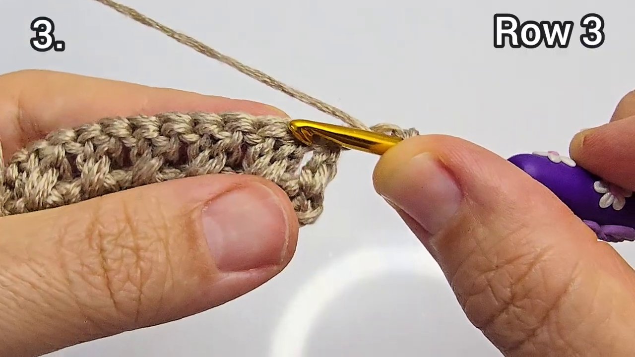 Một bàn ta y đang móc mũi cuối cùng của một dự án, que móc và len tạo thành vòng tròn khép kín.